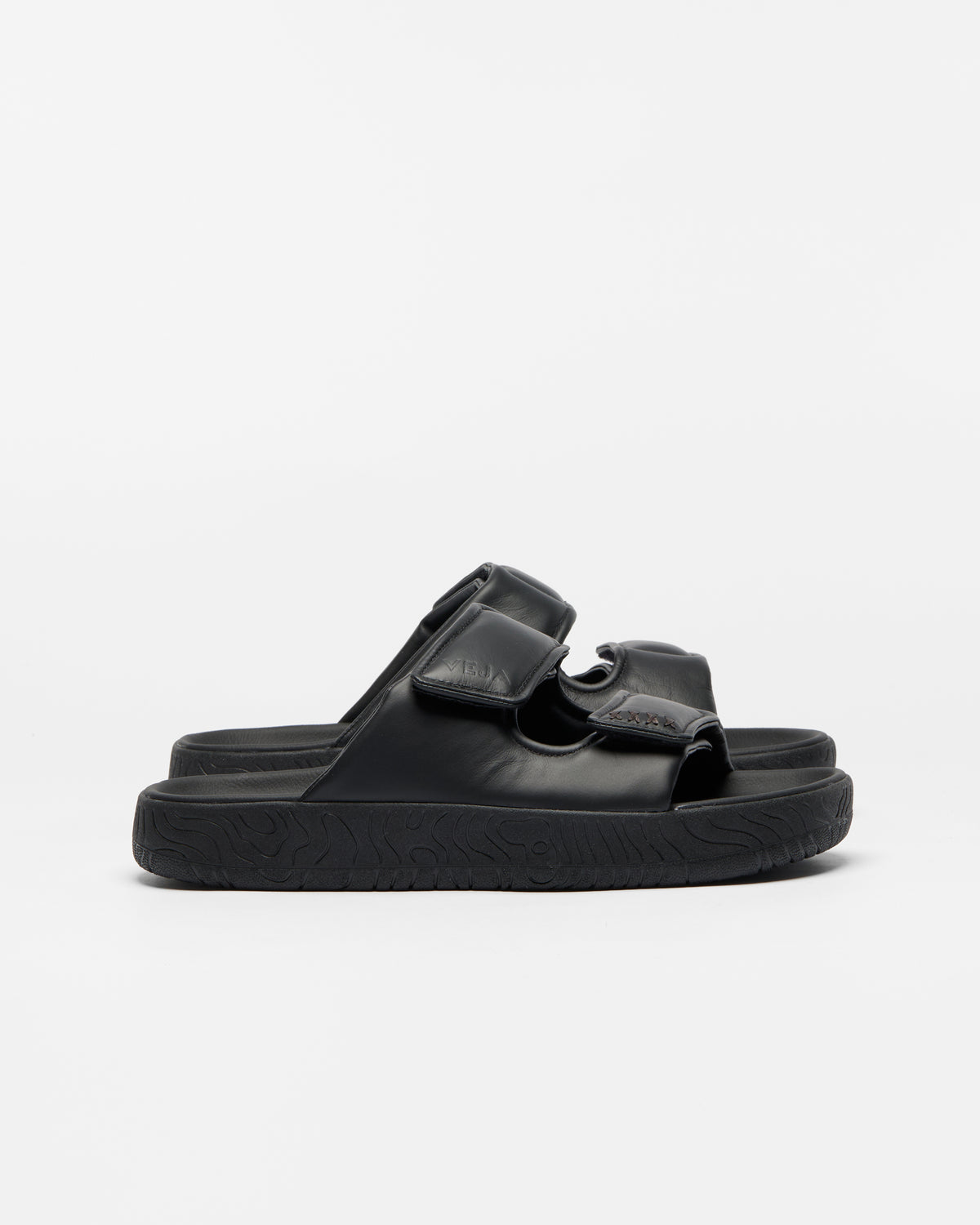 A pair of black double-strap slide sandals with a thick, textured sole, shown from a side profile against a clean white background.