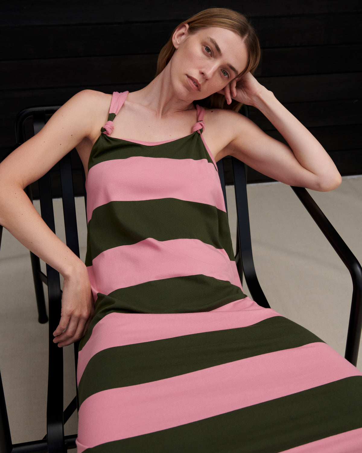 Woman wearing a pink and black striped dress sitting on a chair.