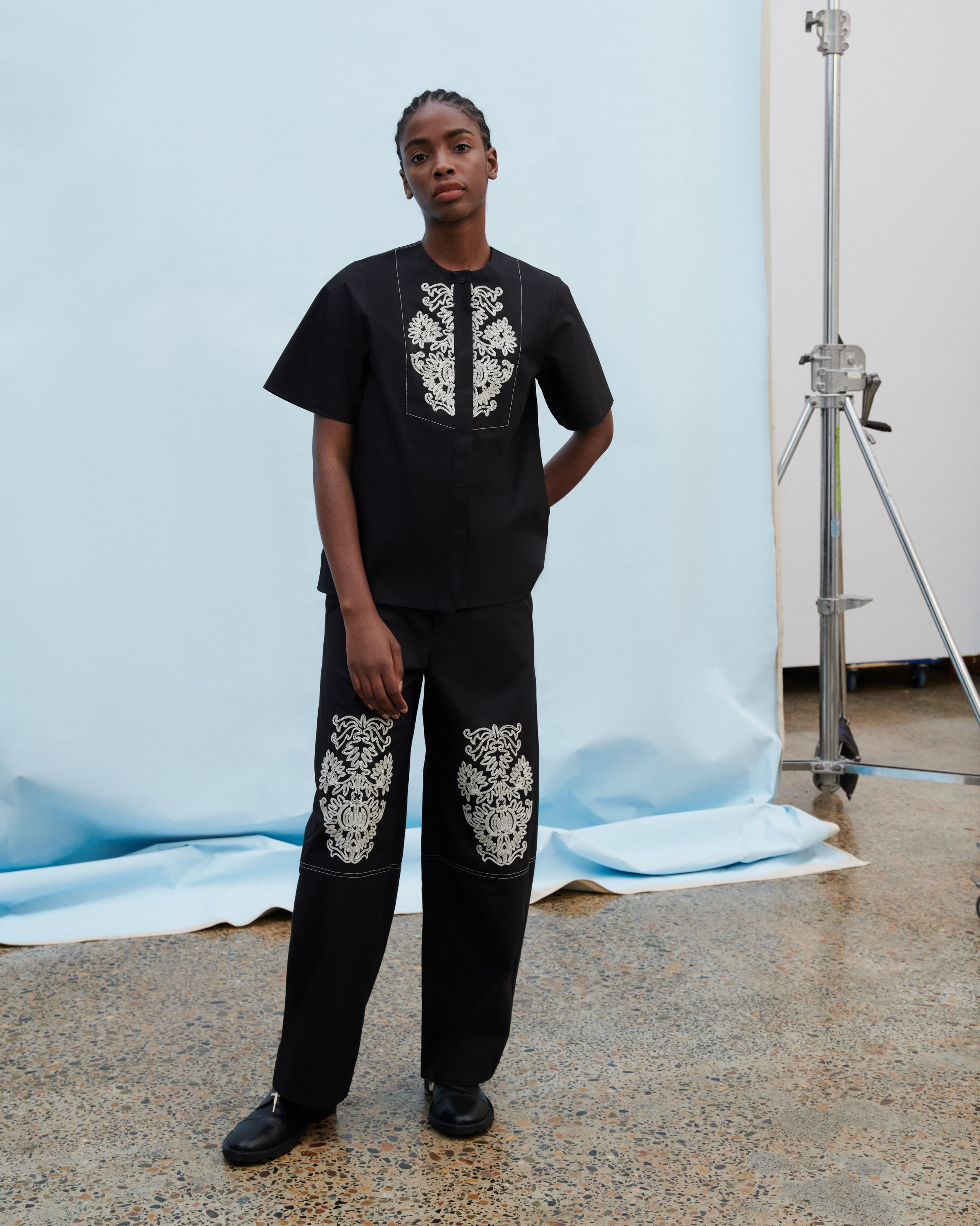 Person wearing a black outfit with white patterns in a studio setting