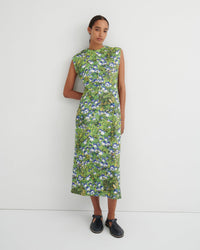A woman modeling a sleeveless midi dress with a green and blue floral print, standing against a plain white studio background.