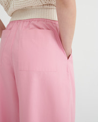 Close-up of a model wearing pink wide-leg trousers with a front patch pocket and a cream ribbed waistband, paired with a cream knit top against a light gray background.