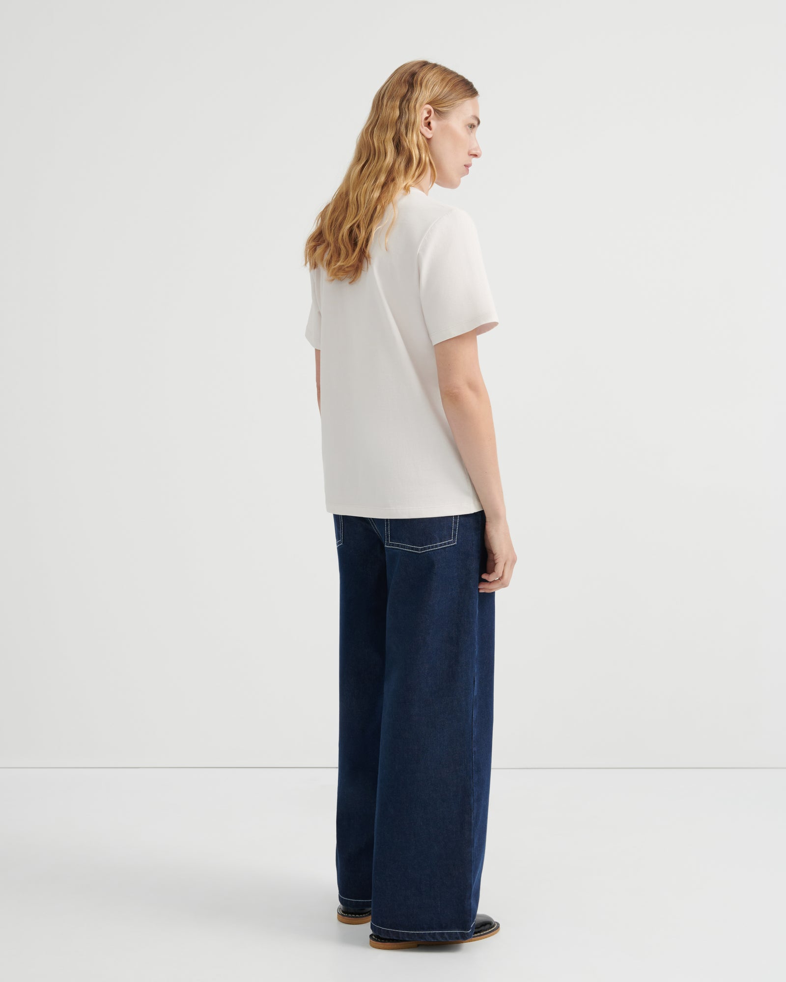 A woman shown from the back wearing a off-white short-sleeve t-shirt and dark blue wide-leg jeans.