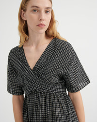 A woman wearing a black and white grid-patterned wrap dress with short puff sleeves and a V-neckline, shown from the chest up against a plain light gray background.