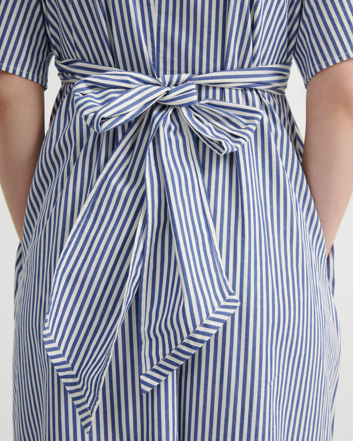 Close-up of a blue and white vertically striped garment with a matching fabric tie belt at the waist, worn by a model.