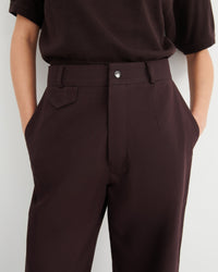 A close-up of a person wearing dark brown tailored trousers and a dark brown short-sleeve top.