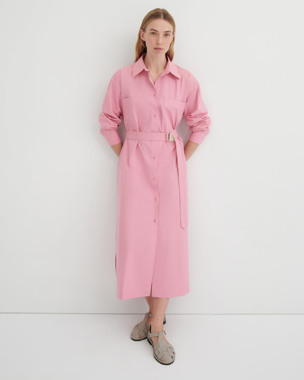 A women wearing a button up pink dress with the sleeves rolled up and the belt cinching the waist.