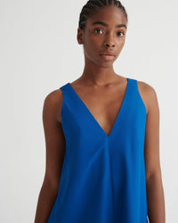 A woman wearing a sleeveless, V-neck blue dress against a plain light gray studio background.