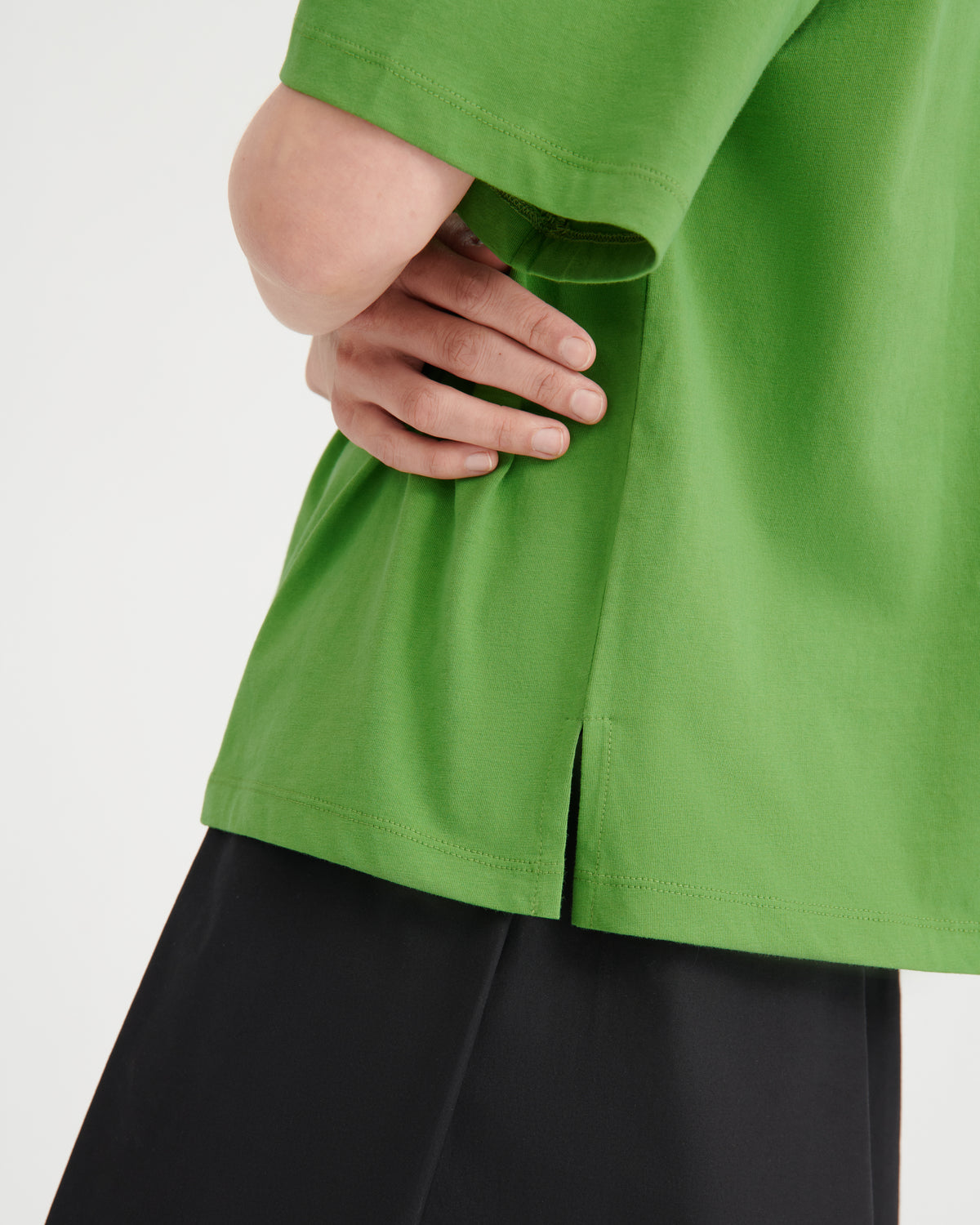 Close-up of a person wearing a bright green short-sleeve top with a side slit hem, paired with black bottoms, against a plain light background.