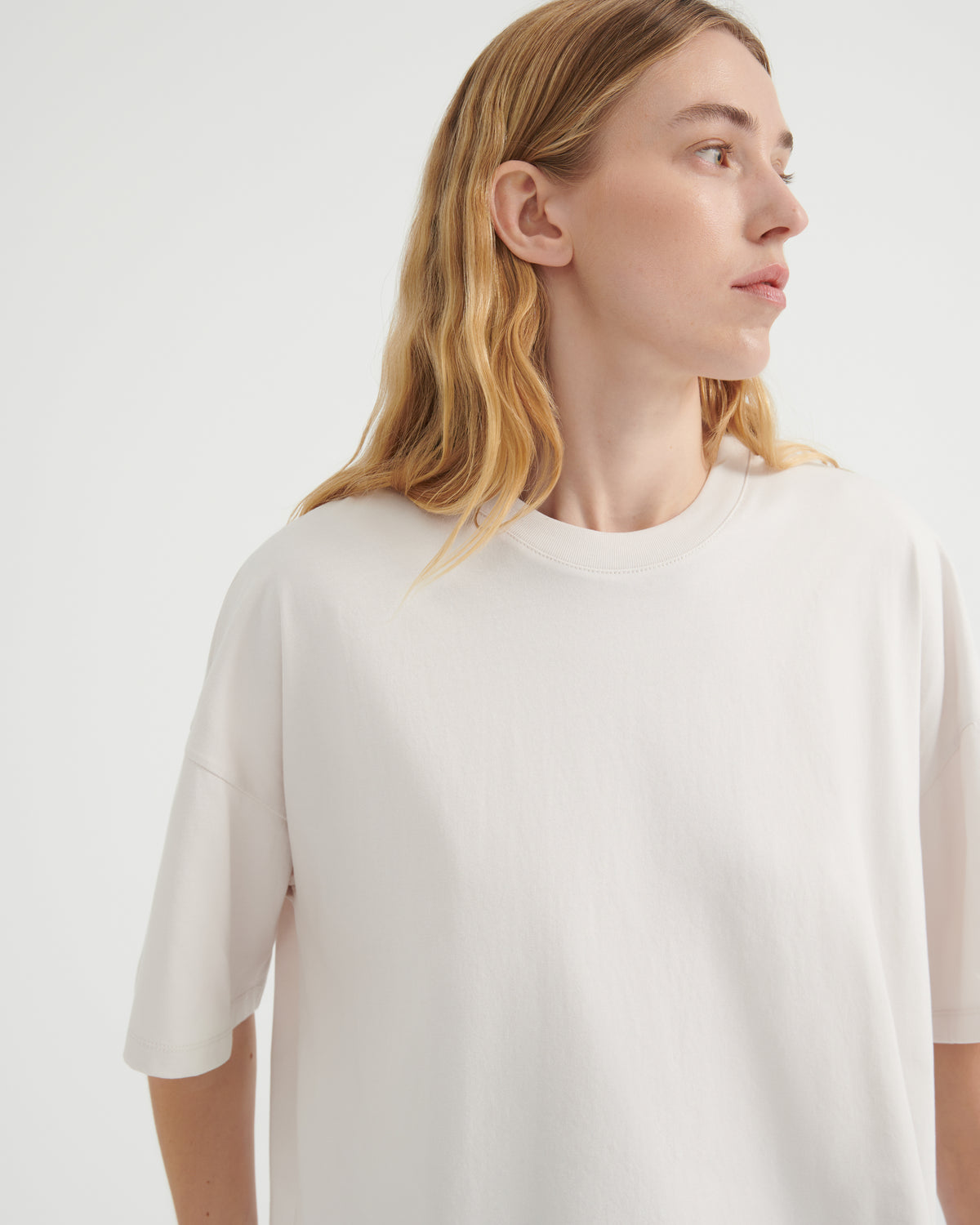 A woman with blonde hair wearing an oversized off-white crewneck t-shirt.