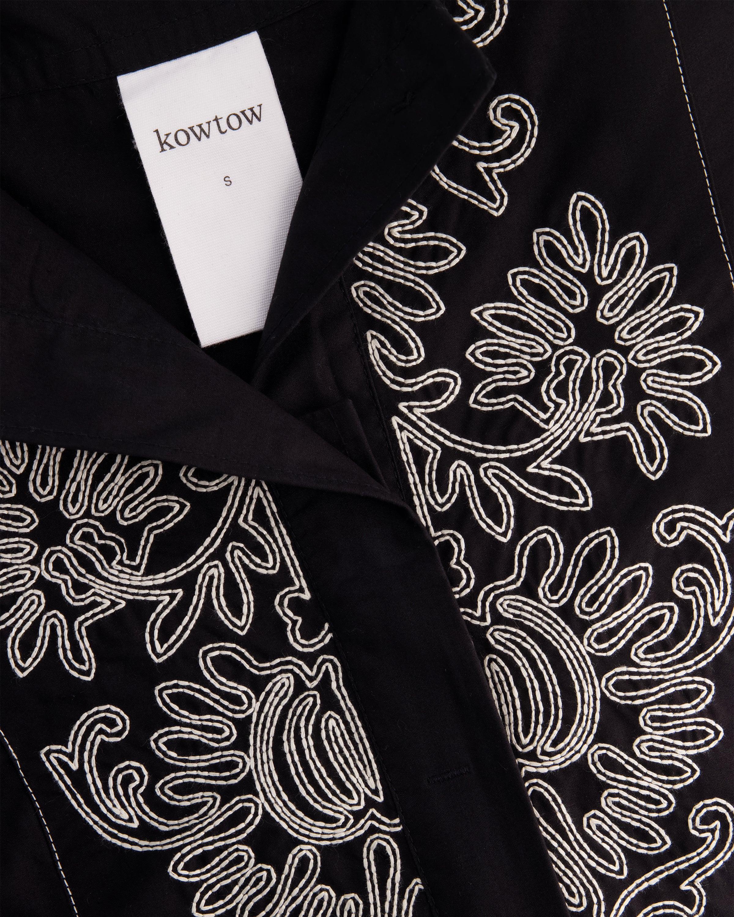 Close-up of a black garment with intricate white embroidered floral and paisley patterns.