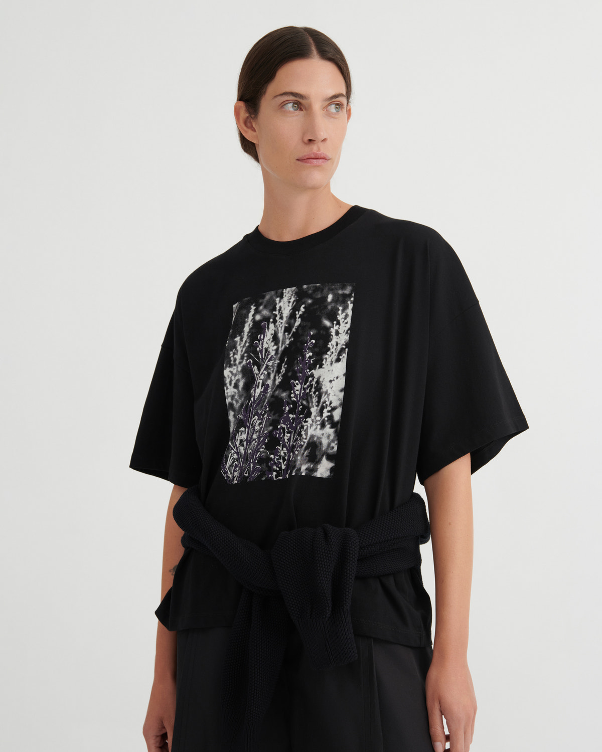 A model wearing a black oversized short-sleeve t-shirt with a square black-and-white abstract graphic print on the front, against a plain light gray studio background.