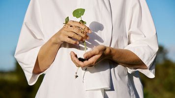 A person holding a seedling wearing an oversized white tee