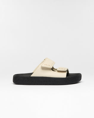 A single slide sandal by Veja, featuring a beige strap with a matching beige logo tab and a thick black textured sole, shown against a plain white studio background.