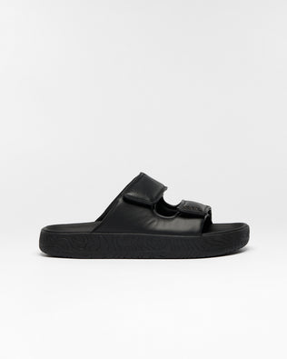 A single black slide sandal with a wide strap and a textured sole, shown in profile against a light gray background.