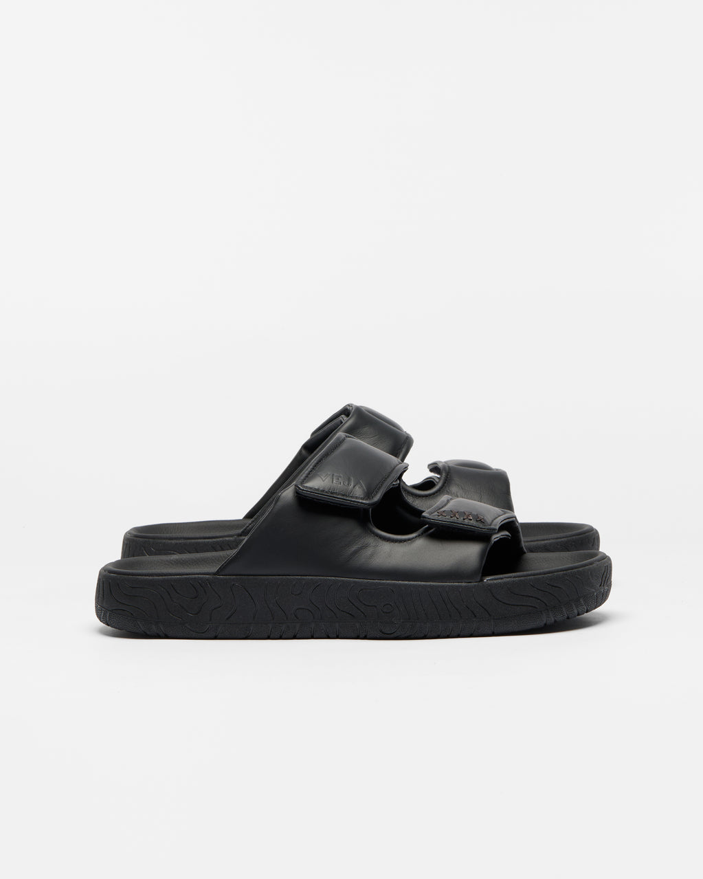 A pair of black double-strap slide sandals with a thick, textured sole, shown from a side profile against a clean white background.