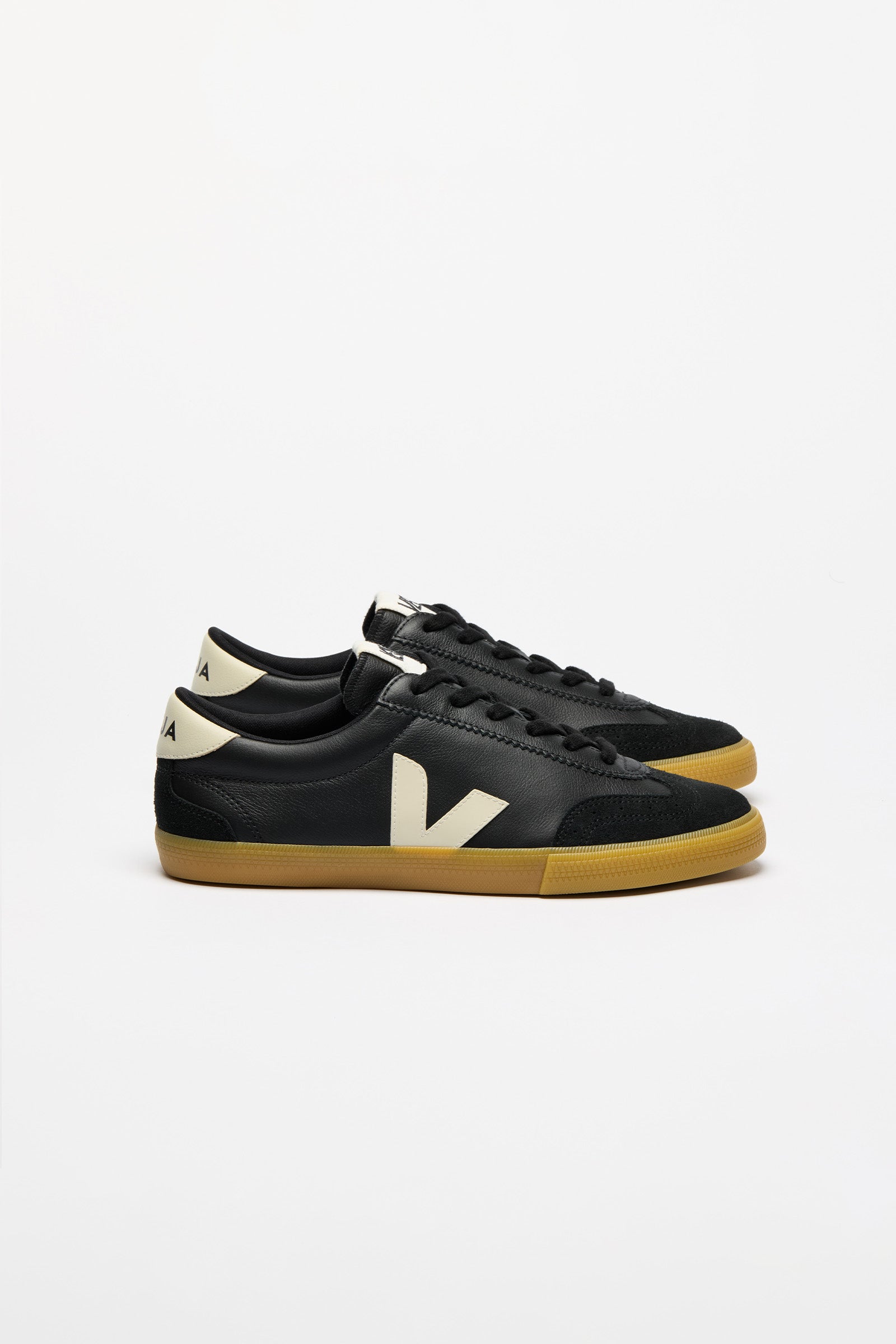 A pair of black leather low-top sneakers with a large cream-colored 'V' logo on the side, cream heel tab, and gum rubber soles.