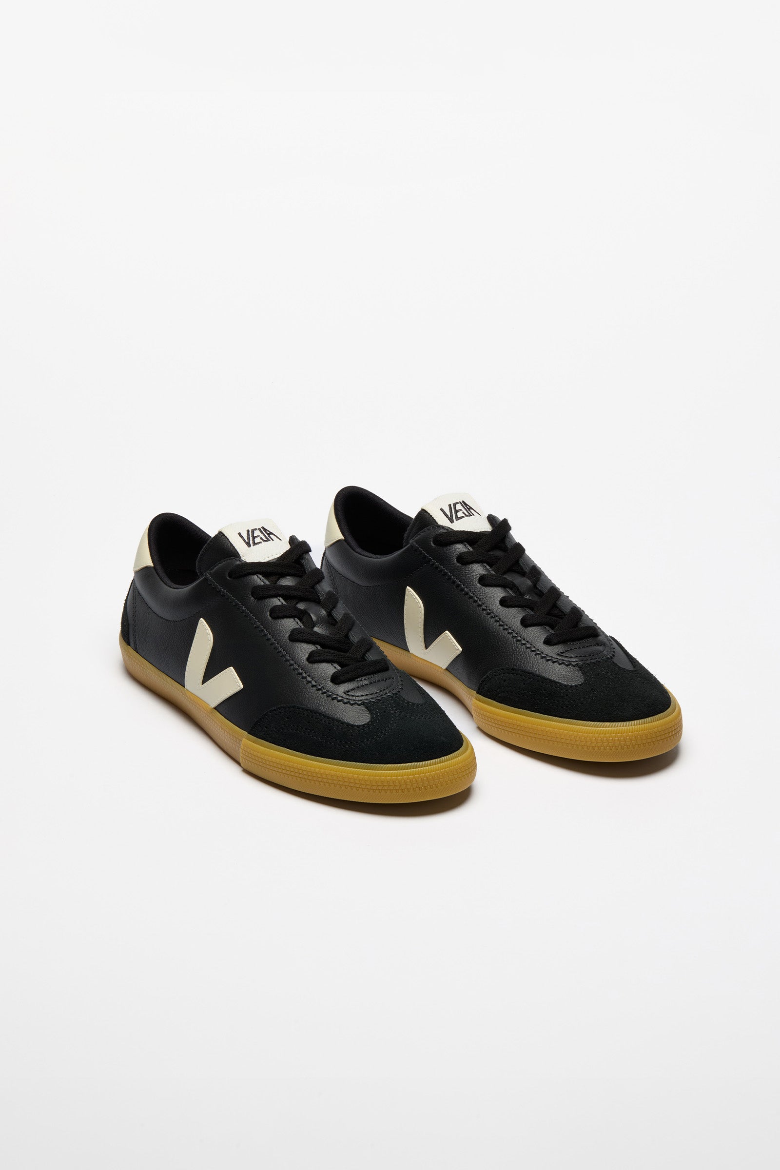 A pair of Veja low-top sneakers in black suede and leather, featuring a signature cream-colored V logo on the side, black laces, and a natural brown gum sole.