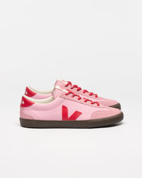 A pair of Veja low-top sneakers in light pink suede and leather, featuring a bold red 'V' logo, red laces, and a dark brown rubber sole.