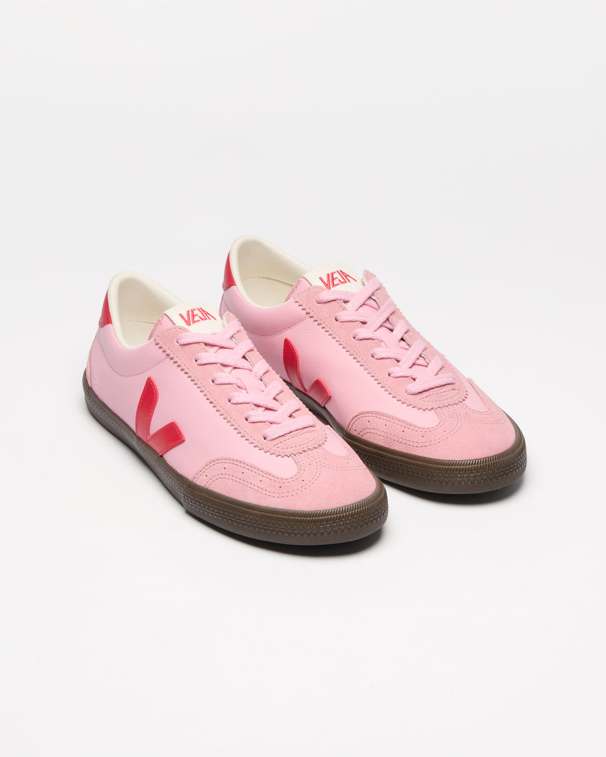 A pair of pink low-top sneakers with red side stripes and brown gum soles.