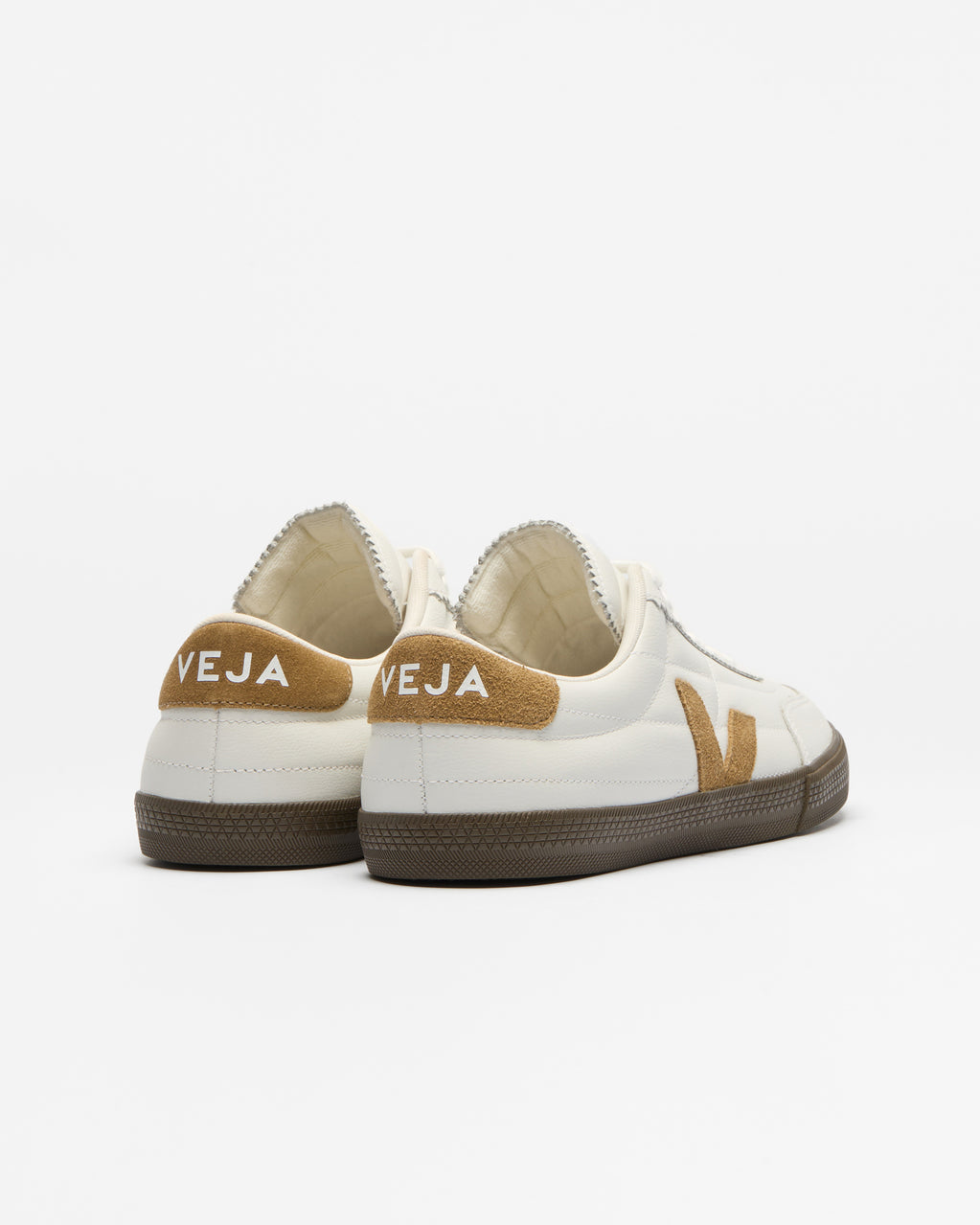 A pair of Veja low-top sneakers shown from the back, featuring an off-white leather upper, tan suede heel tabs with the brand name 'VEJA' in white, and dark brown rubber soles.
