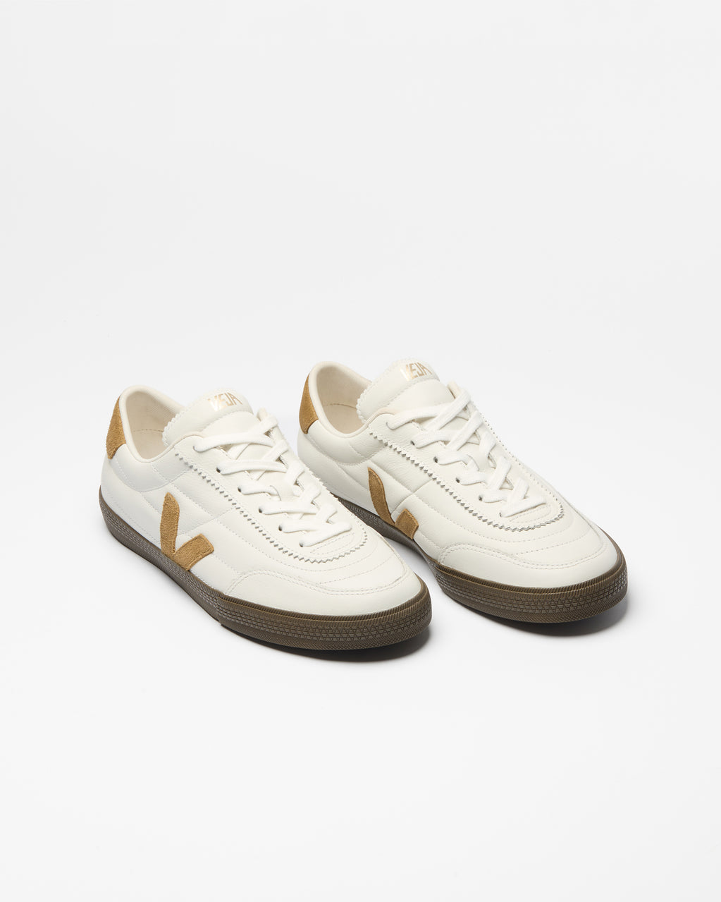 A pair of low-top sneakers in off-white leather with tan side stripes and heel accents, dark brown soles, and white laces.