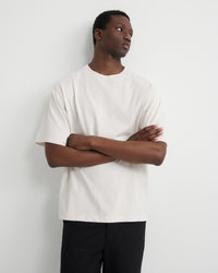 A man wearing an oversized off-white short-sleeve t-shirt and black pants.