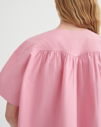 Close-up back view of a person wearing a loose pink short-sleeve top with gathered shoulder seams, against a plain light background.