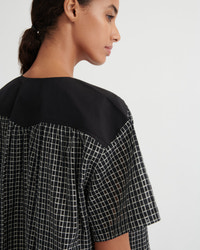 Close-up side profile of a woman wearing a loose black and white checkered top with a solid black yoke collar, against a plain light gray background.