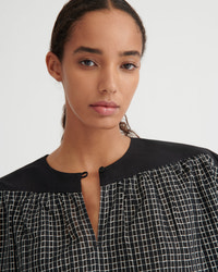 A close-up of a model wearing a black and white checkered top with a solid black collar and button placket, set against a plain light gray background.