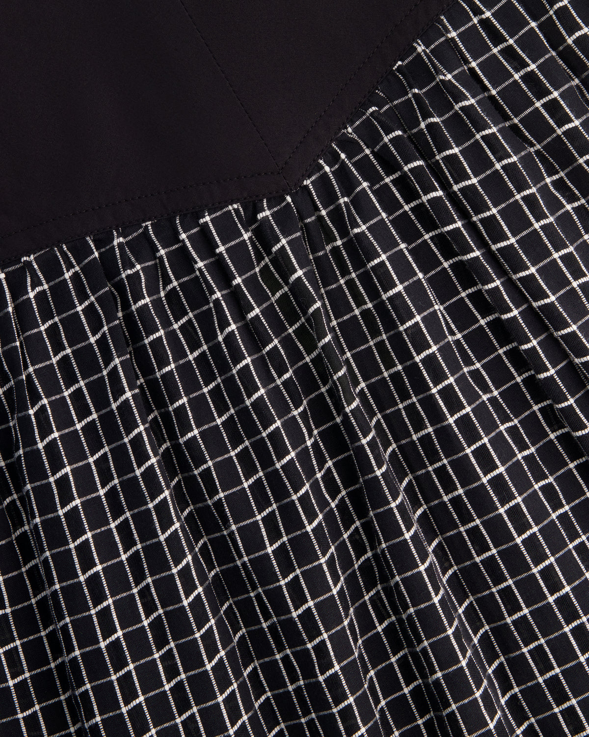 Close-up of a black garment with a white grid pattern and a solid black yoke or upper section.