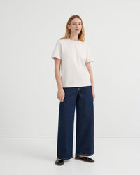 A woman modeling a off-white short-sleeve crewneck t-shirt and dark blue wide-leg jeans.