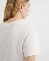 A close-up side profile of a woman wearing a plain off-white short-sleeve crewneck t-shirt.