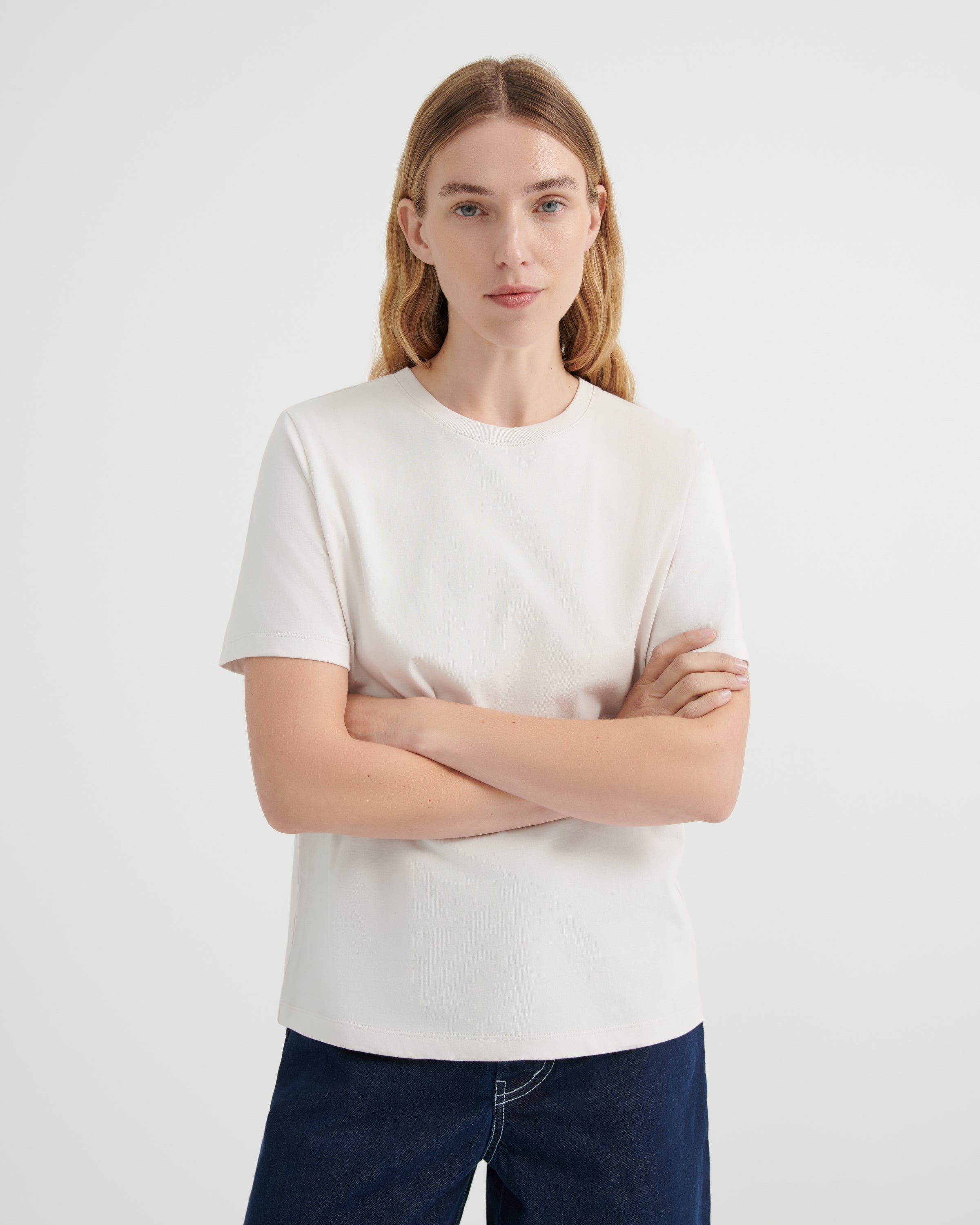 A woman wearing a plain off-white short-sleeve crewneck t-shirt and dark blue jeans.
