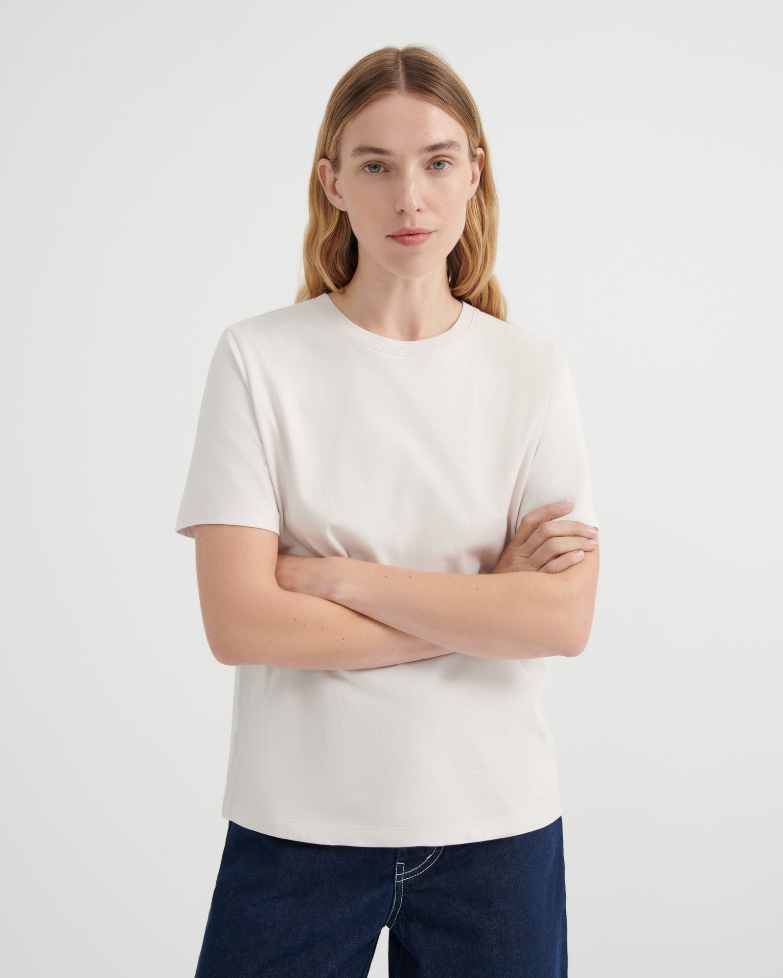 A woman wearing a plain off-white short-sleeve crewneck t-shirt and dark blue jeans.