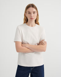 A woman wearing a plain off-white short-sleeve crewneck t-shirt and dark blue jeans.