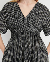 A close-up of a woman wearing a black and white grid-patterned wrap dress with short sleeves and a V-neckline.