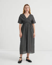 A woman modeling a short-sleeve wrap-style midi dress with a black and white micro-check pattern, standing against a plain light gray studio background.