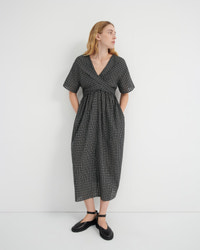 A woman modeling a short-sleeve black and white checkered midi dress with a wrap-style V-neck and side pockets, paired with black Mary Jane shoes, against a plain white studio background.