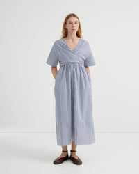 A woman modeling a blue and white vertically striped midi dress with short sleeves, a V-neckline, and a gathered waist, set against a plain white studio background.