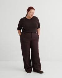 A woman modeling a dark brown short-sleeve top and matching wide-leg trousers against a plain light gray studio background.
