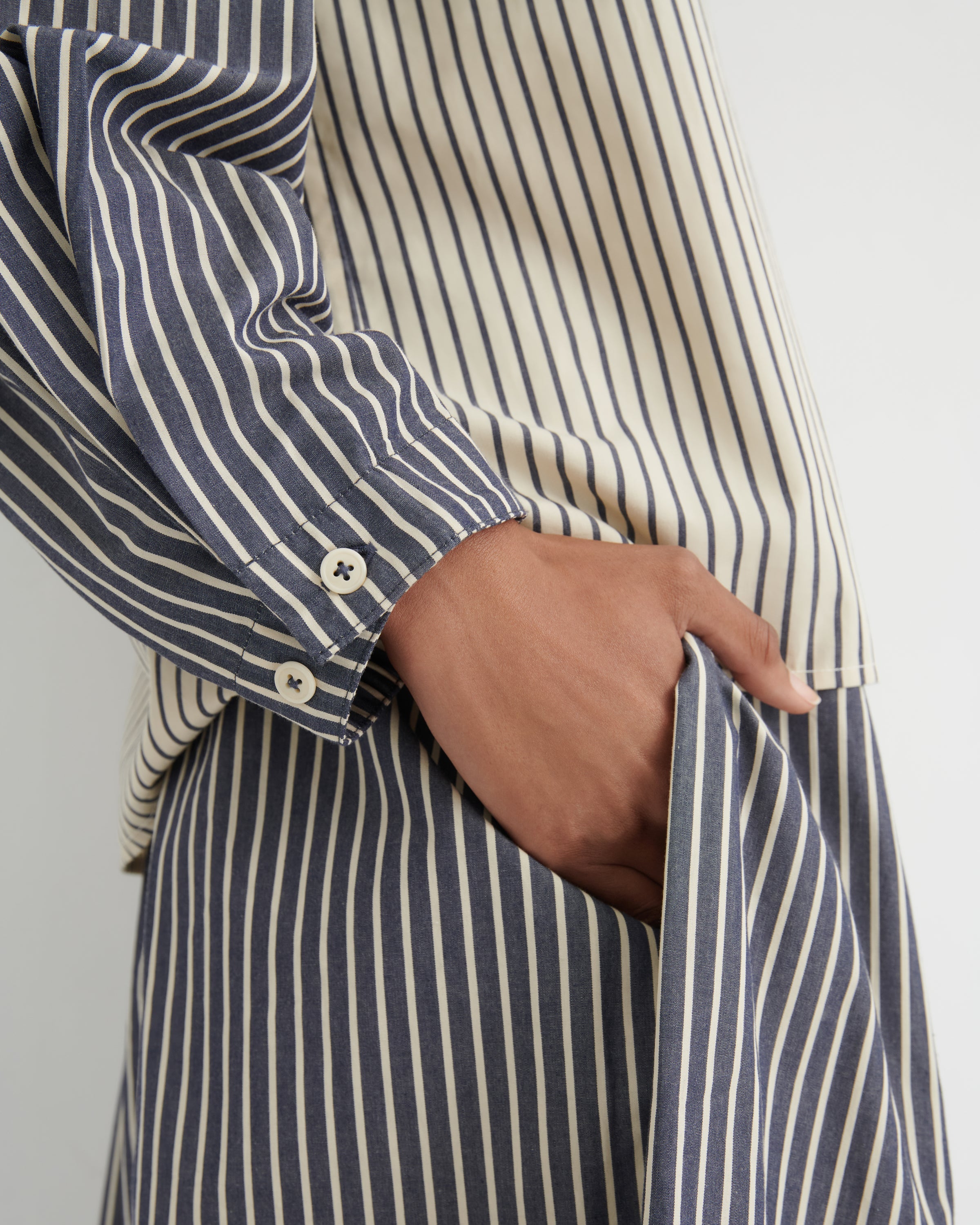 Close-up of a person wearing a navy and cream vertically striped shirt and matching striped trousers, with one hand tucked into a pocket.