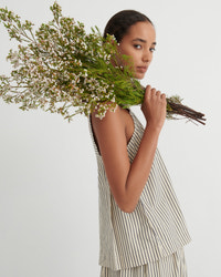 A model wearing a sleeveless, tiered top and matching bottoms in a beige and black striped pattern, holding a large bouquet of baby's breath flowers against her shoulder, set against a plain light gray background.
