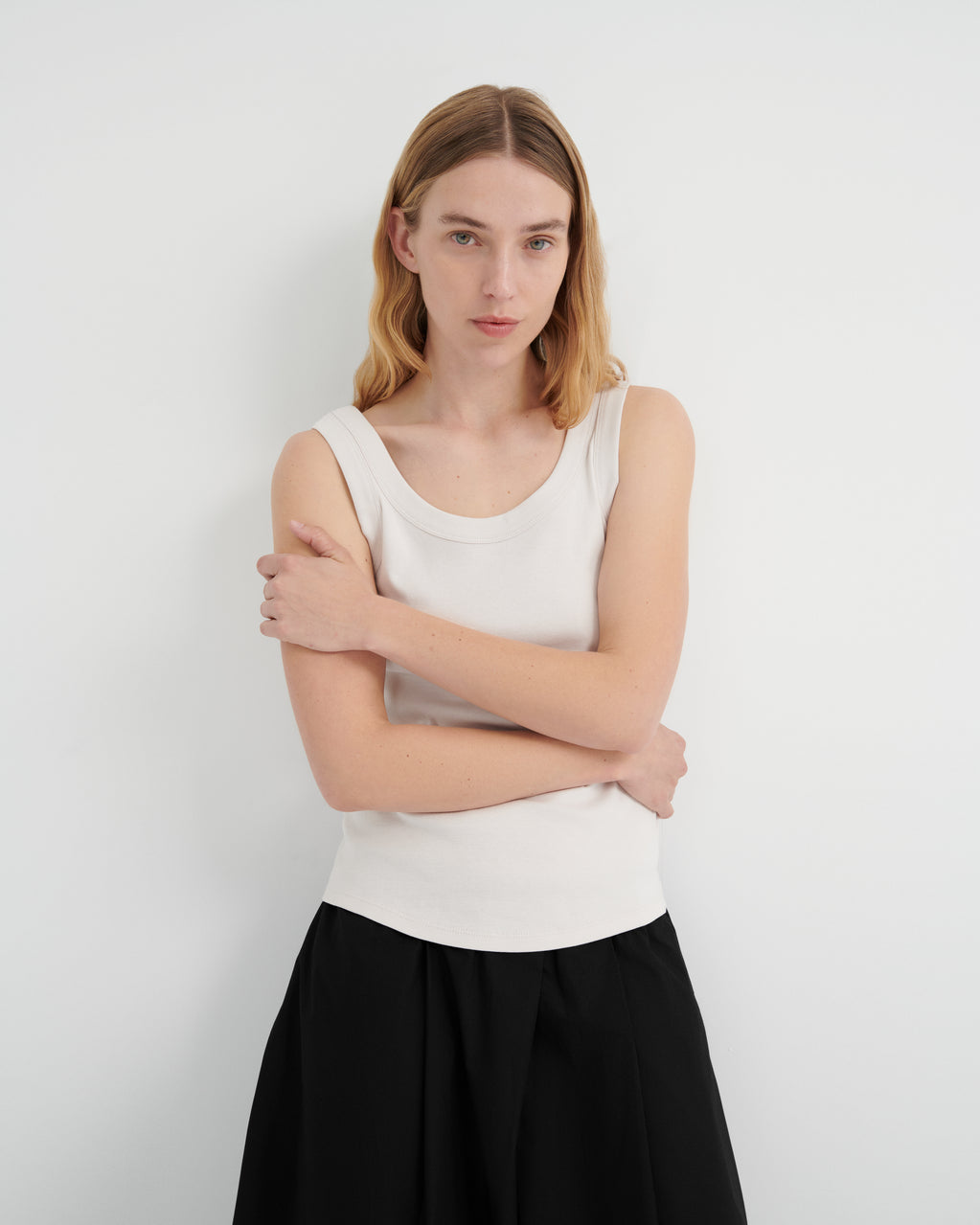 A woman wearing a white ribbed scoop-neck tank top and black culottes.