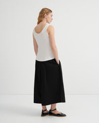 A woman shown from the back wearing a white ribbed tank top and black culottes paired with black flat sandals.