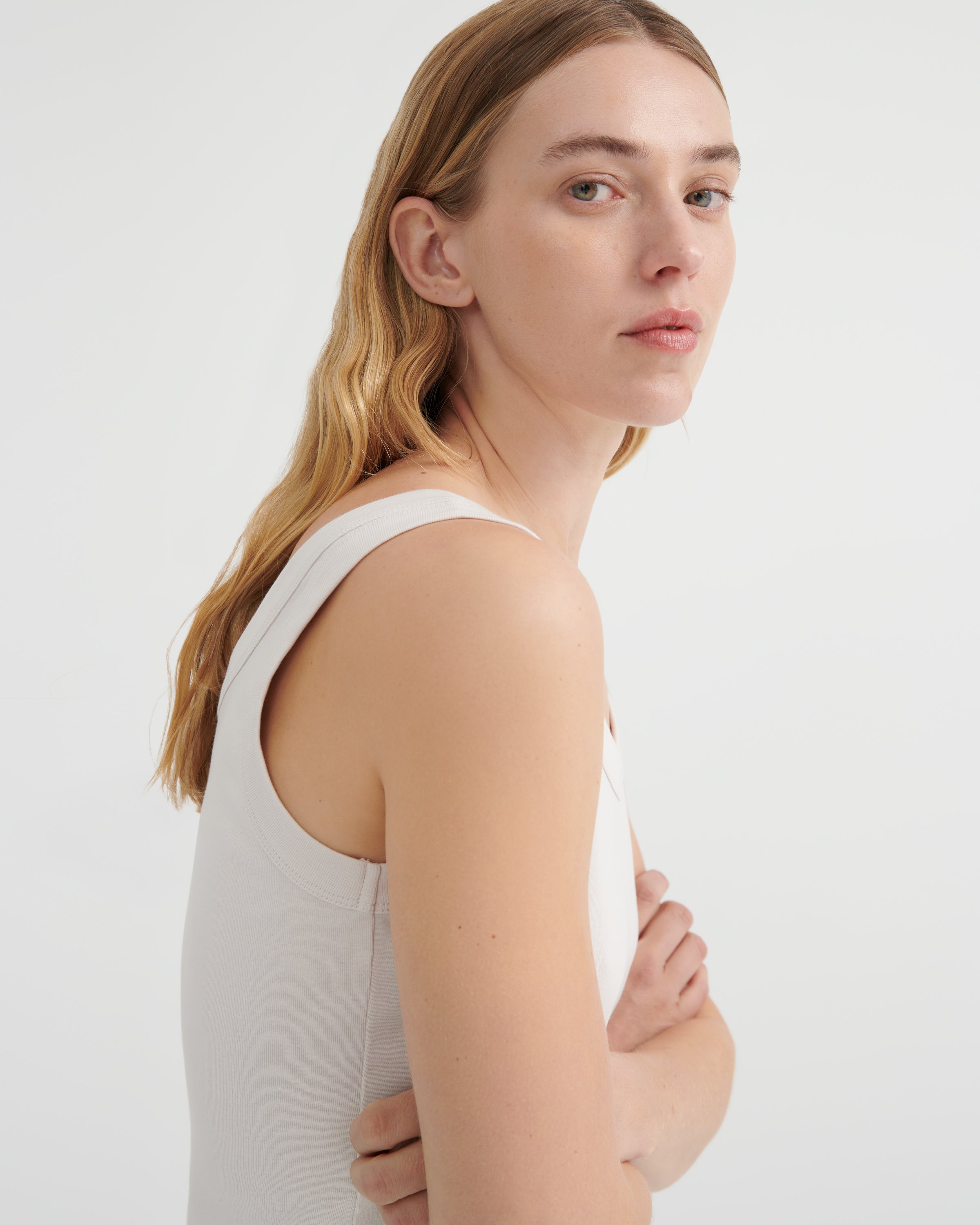 A woman shown from a side-back angle wearing a light beige sleeveless tank top.