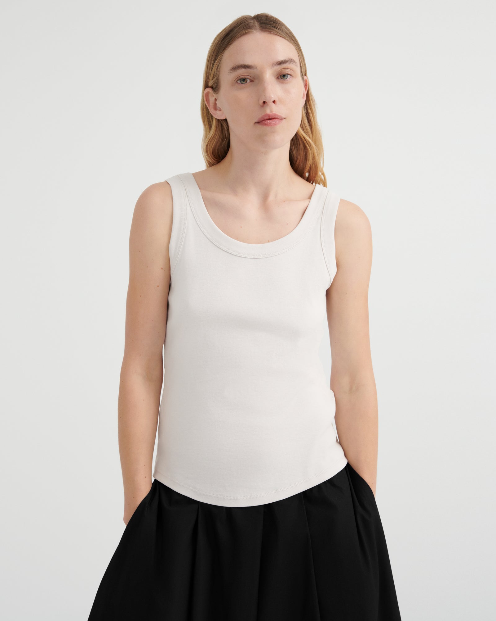 A woman modeling a fitted sleeveless scoop-neck tank top in off-white, paired with black culottes.