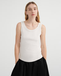 A woman modeling a fitted sleeveless scoop-neck tank top in off-white, paired with black culottes.