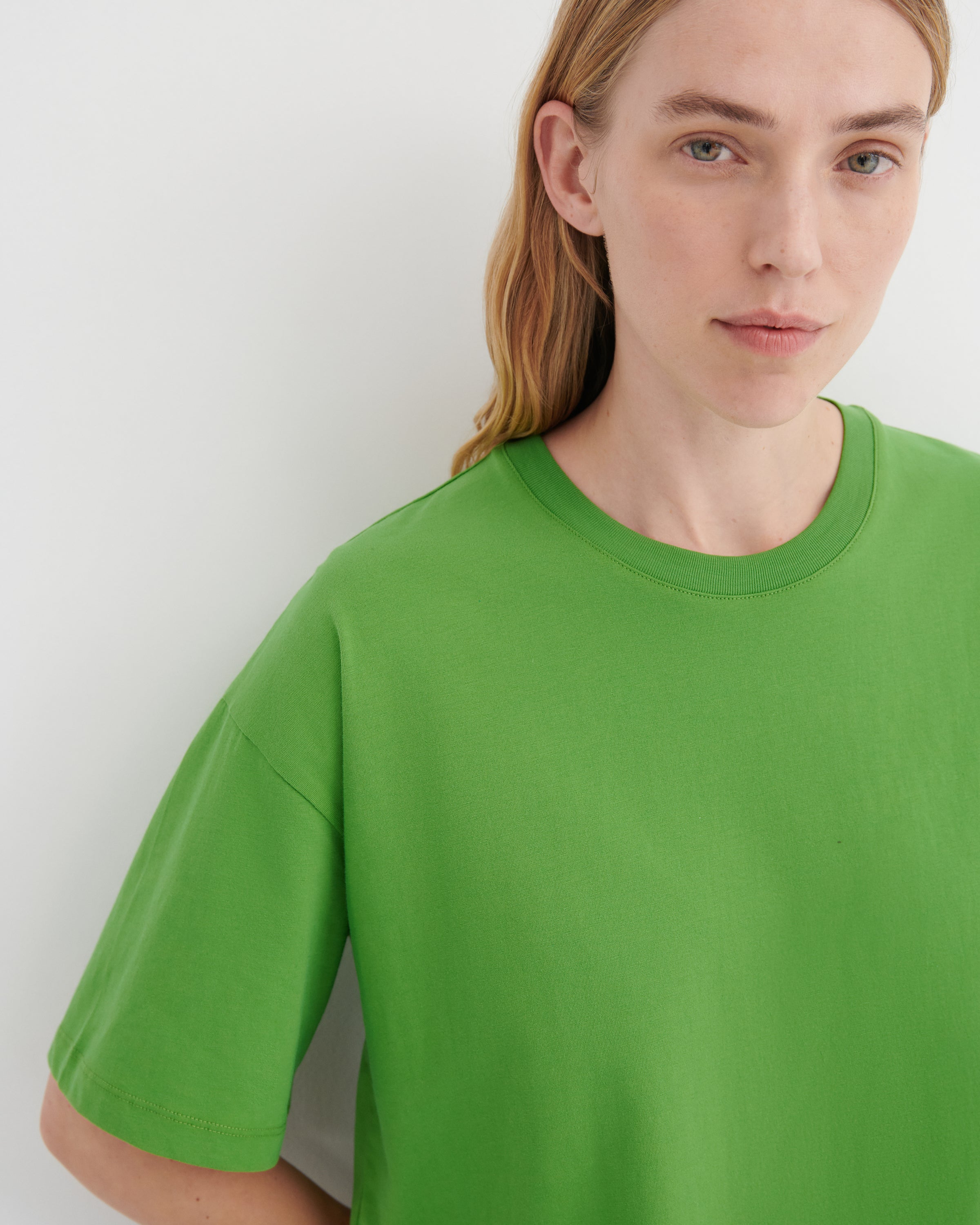 A close-up of a model wearing a bright green crewneck t-shirt against a plain light gray background.