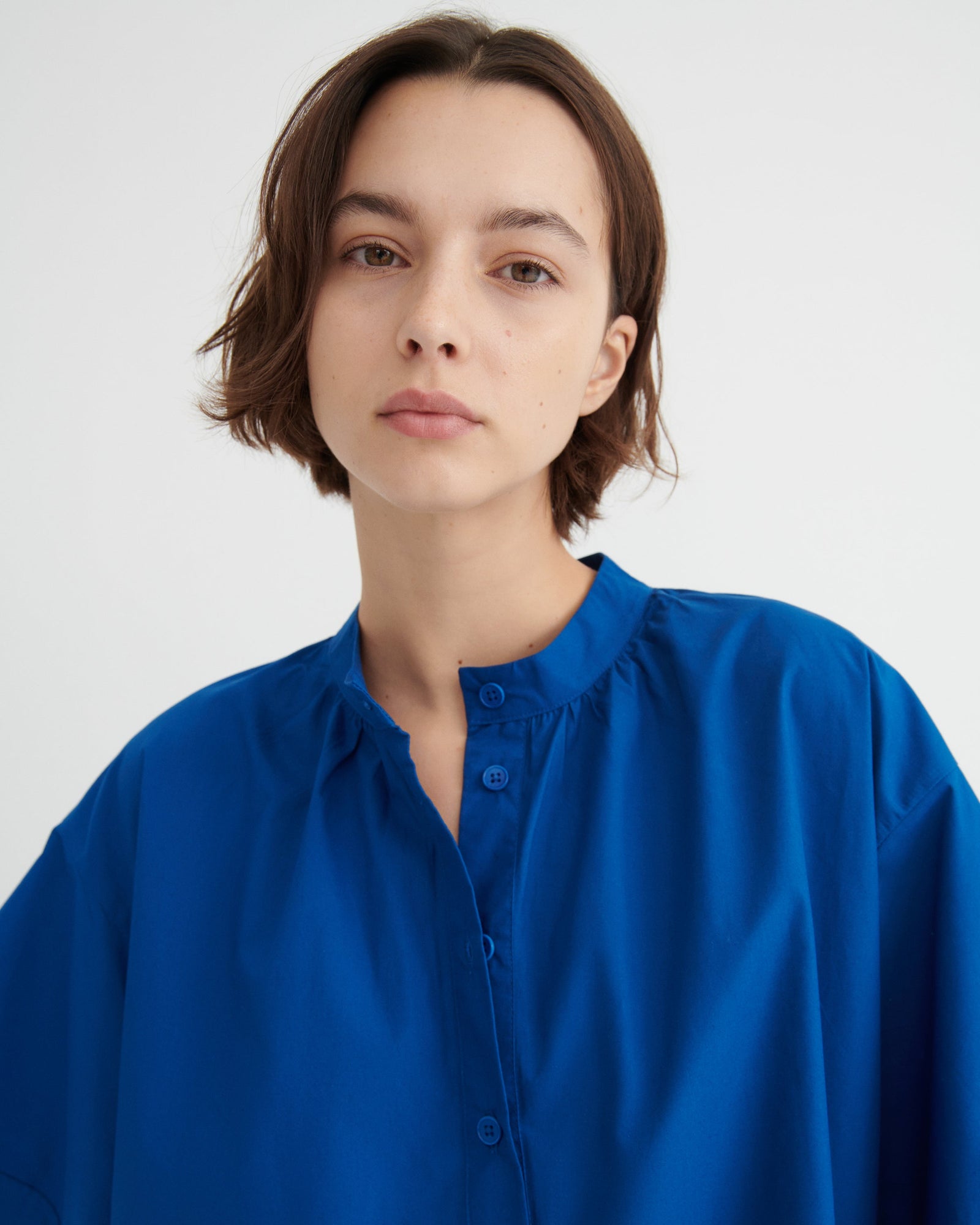 A woman with short brown hair wearing a vibrant royal blue button-up dress.