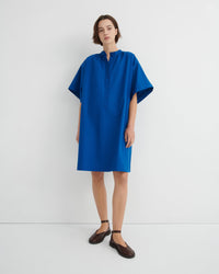 A woman modeling a loose-fitting, short-sleeved blue dress with a buttoned mock neck.